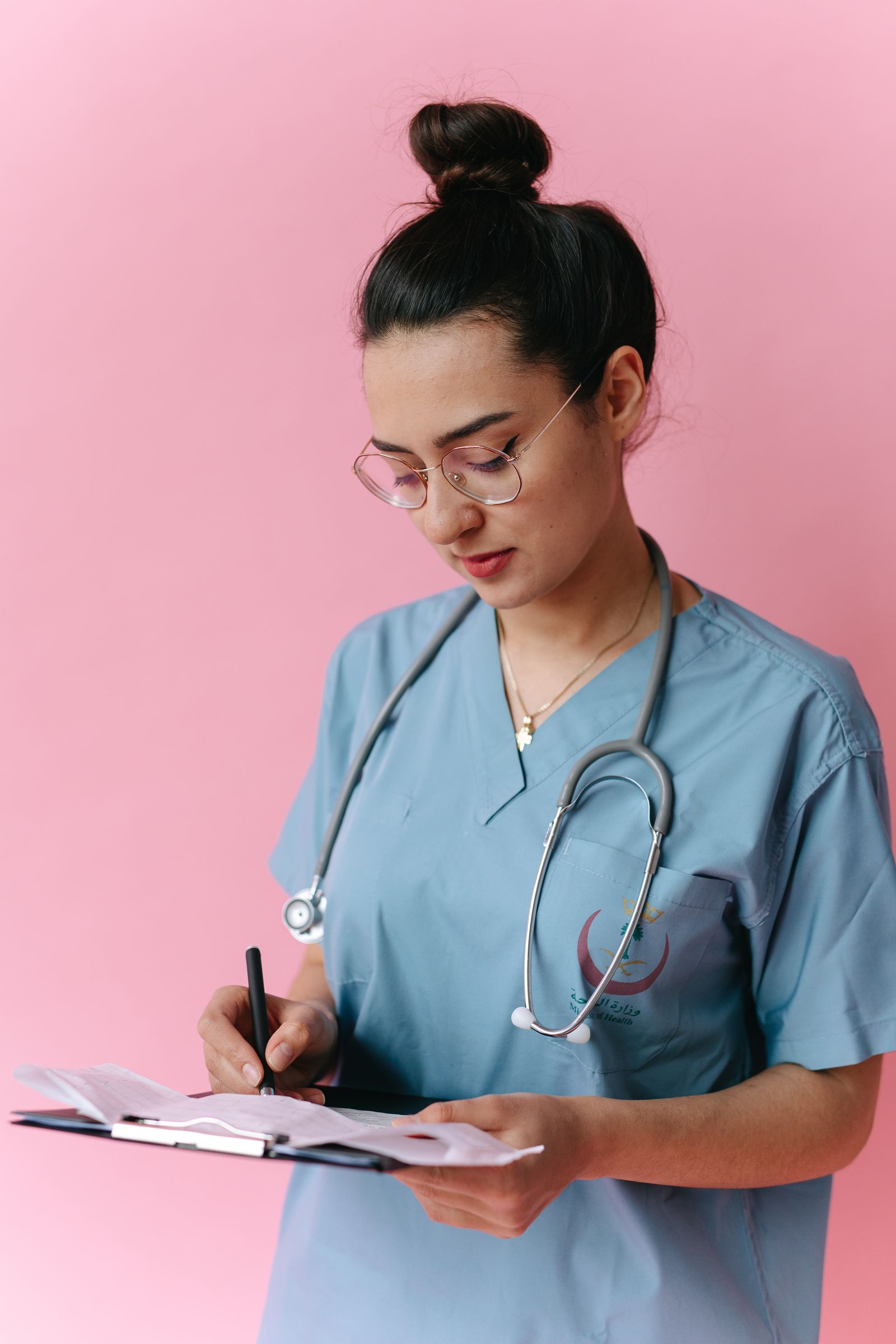Young adult nurse in blue scrubs writing on a clipboard